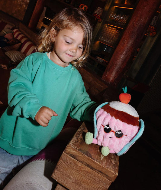 Fille debout tenant la peluche originale Cherry Cake posée sur une rampe - vue de face - Hello Hossy