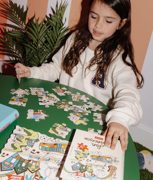 Fille assemblant le puzzle coloré 16 pièces "San Francisco" sur une table – vue de face – Hello Hossy